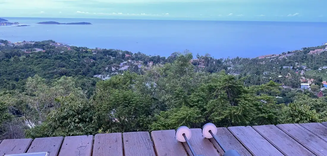 View from a hillside wooden deck over trees, the Samui coast and the sea